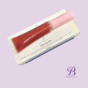 Cherry lip gloss bath bomb beauties Pink lip gloss tube resting on white packaging with cherry lip gloss branding on a pastel lavender background bath bomb beauties logo visible in corner