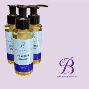 Three Bath Bomb Beauties oil-to-milk cleansers with black pump tops on a lavender background, front label reads 'Oil To Milk Cleanser'.