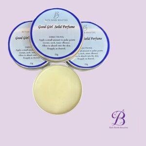 Close-up of blue-labeled bath bomb tins reading 'Good Girl Solid Perfume' with a pale purple background.