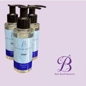 Three Bath Bomb Beauties toner bottles with blue labels and black pump tops, arranged in front of a lavender backdrop with part of the brand logo visible.