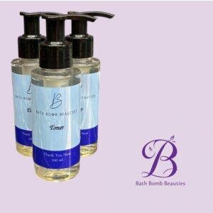 Three pump bottles labeled Bath Bomb Beauties Toner on a lavender background; brand logo visible in the corner.