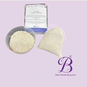 Bath Bomb Beauties products on lavender background: bowl of bath mixture, a labeled packet, and a beige drawstring bag near the logo.