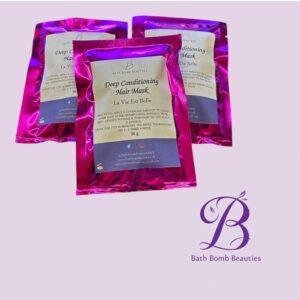 Three pink foil Deep Conditioning Hair Mask packets from Bath Bomb Beauties on a lavender background with their logo visible at bottom right.