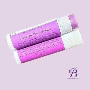 Two purple raspberry blue lip balm tubes angled on a pale lavender background with bath bomb beauties branding visible in the corner