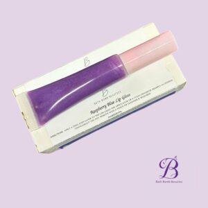 Purple lip gloss tube with pink cap labeled raspberry blue lip gloss resting on a white box against a lavender background bath bomb beauties logo visible