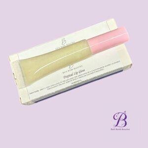 Two lip gloss tubes in pink and gold rest diagonally on a white box with bath bomb beauties branding against a pale lavender background