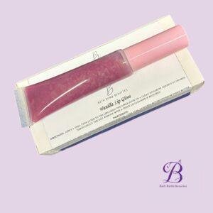 Pink vanilla lip gloss tube with pink cap on its white packaging against a pastel purple background bath bomb beauties branding