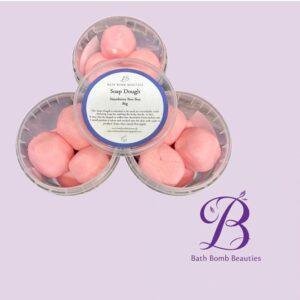 Three clear plastic containers of pink soap dough balls arranged in a triangle on a lavender background with a central label reading soap dough by bath bomb beauties