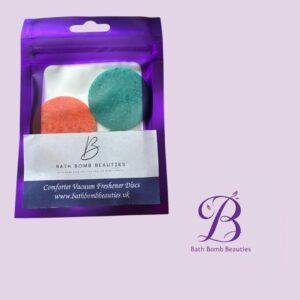 Purple resealable bag with two round bath bombs (orange and teal) and a product label on a lavender background; Bath Bomb Beauties logo.