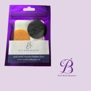 Purple resealable bag showing two discs (orange and black) labeled 'Gold Orchid Vacuum Freshener Discs' from Bath Bomb Beauties; brand logo in bottom right.