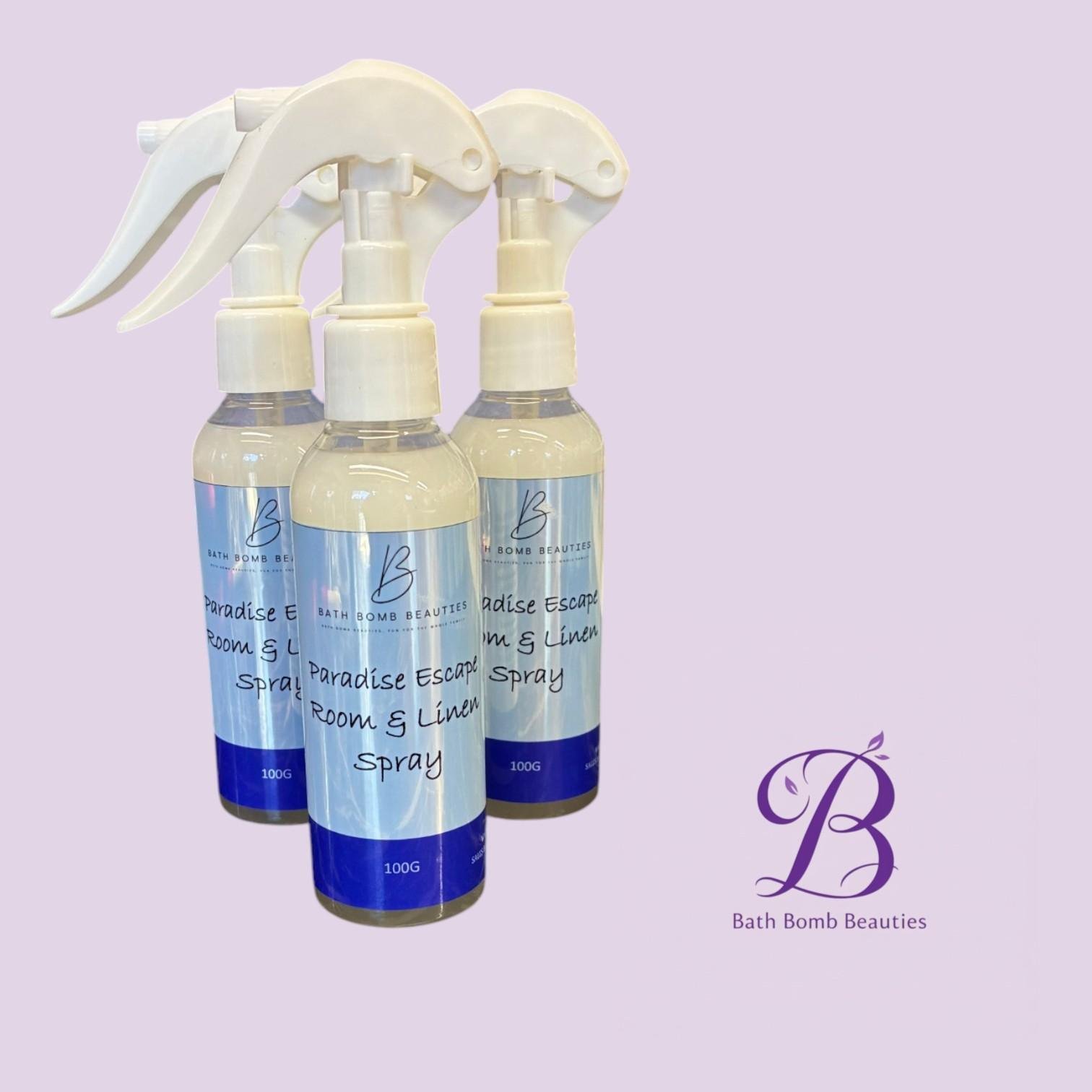 Paradise escape bath bomb beauties Three white spray bottles labeled bath bomb beauties paradise escape room linen spray on a lavender background with a purple logo in the corner