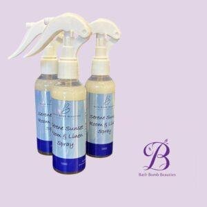 Three spray bottles labeled bath bomb beauties serene sunset room  linen spray on a lavender background with a corner logo