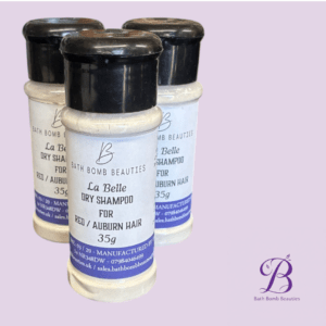 Three small bottles of Bath Bomb Beauties La Belle Dry Shampoo for red/auburn hair against a light purple background, logo bottom right.