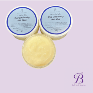 Three jars of Bath Bomb Beauties La Vie Est Belle Deep Conditioning Hair Mask, two closed with blue lids and one open showing pale yellow cream, on a lavender background with a purple Bath Bomb Beauties logo in the corner.